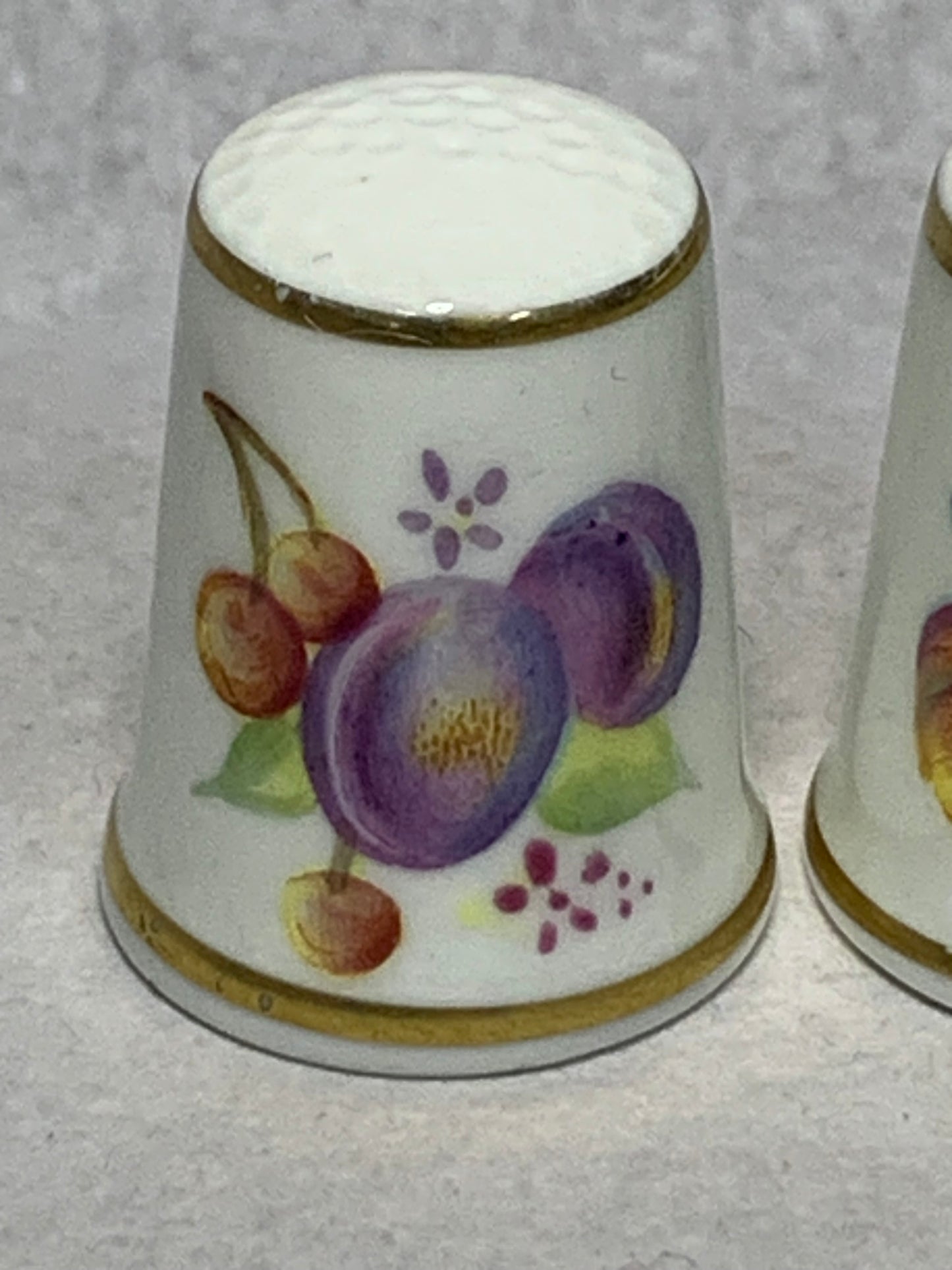 Pair of Royal Worcester fine bone china thimbles, hand-painted with fruit still-life designs (plums, cherries, apricots, and berries) on a white ground with gilt rims 1951