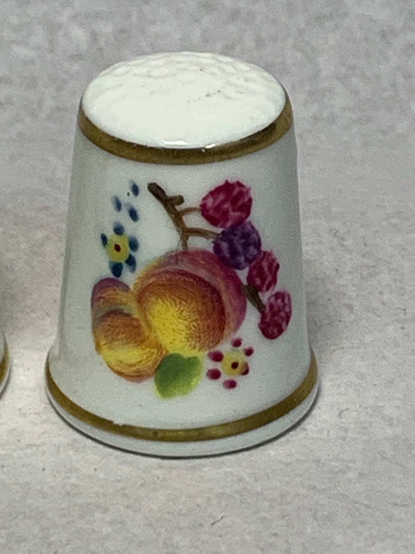 Pair of Royal Worcester fine bone china thimbles, hand-painted with fruit still-life designs (plums, cherries, apricots, and berries) on a white ground with gilt rims 1951