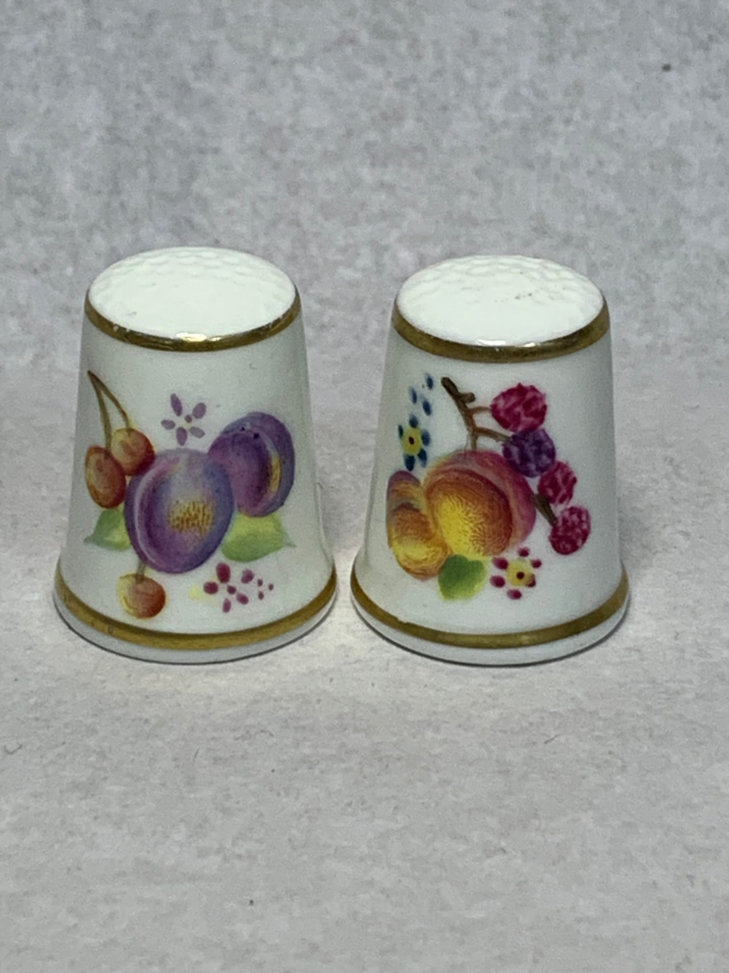 Pair of Royal Worcester fine bone china thimbles, hand-painted with fruit still-life designs (plums, cherries, apricots, and berries) on a white ground with gilt rims 1951