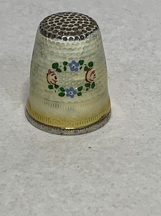 Antique metal thimble with hand-painted enamel floral decoration — a wreath of pink roses and blue forget-me-nots with green leaves encircling the body, set against a cream/ivory enameled ground