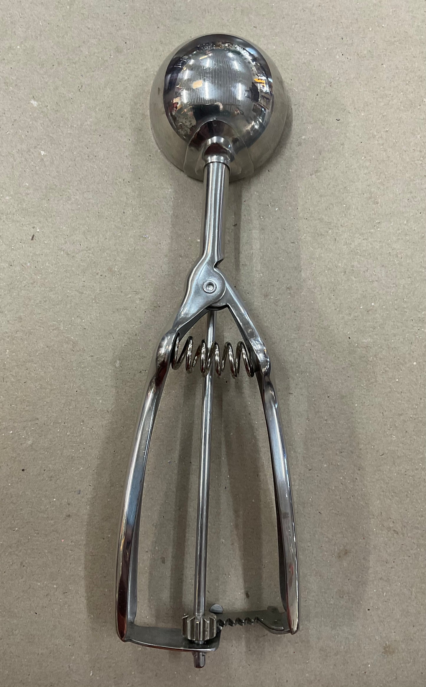 Vintage stainless steel ice cream scoop with spring-loaded handle and scraper mechanism