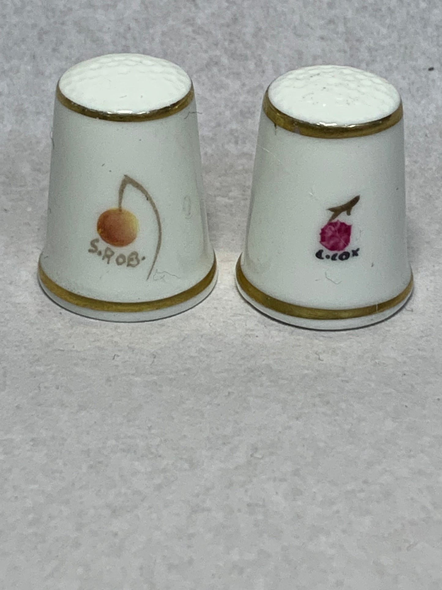 Pair of Royal Worcester fine bone china thimbles, hand-painted with fruit still-life designs (plums, cherries, apricots, and berries) on a white ground with gilt rims 1951