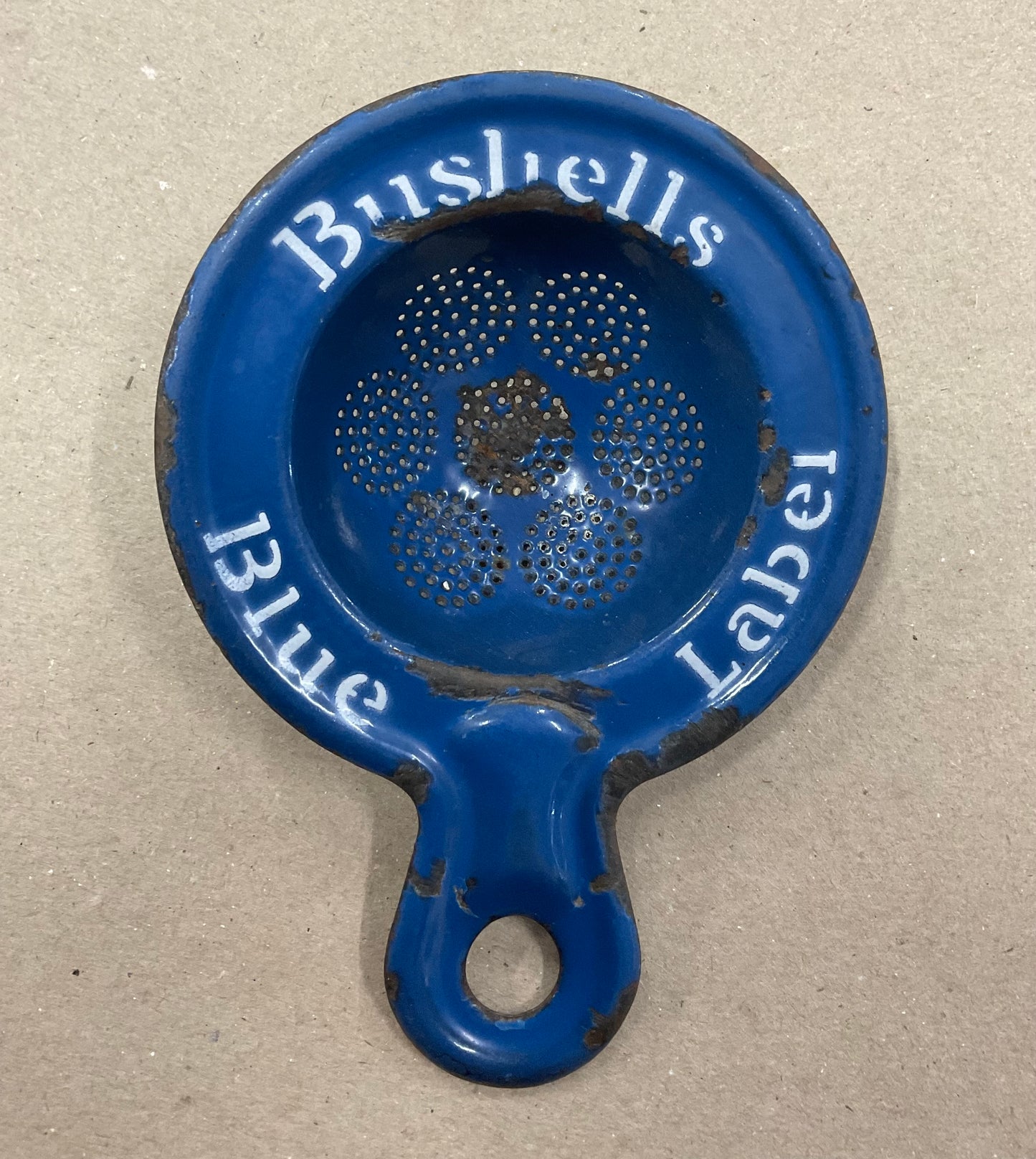 A vintage enamel tea strainer advertising Bushells Blue Label